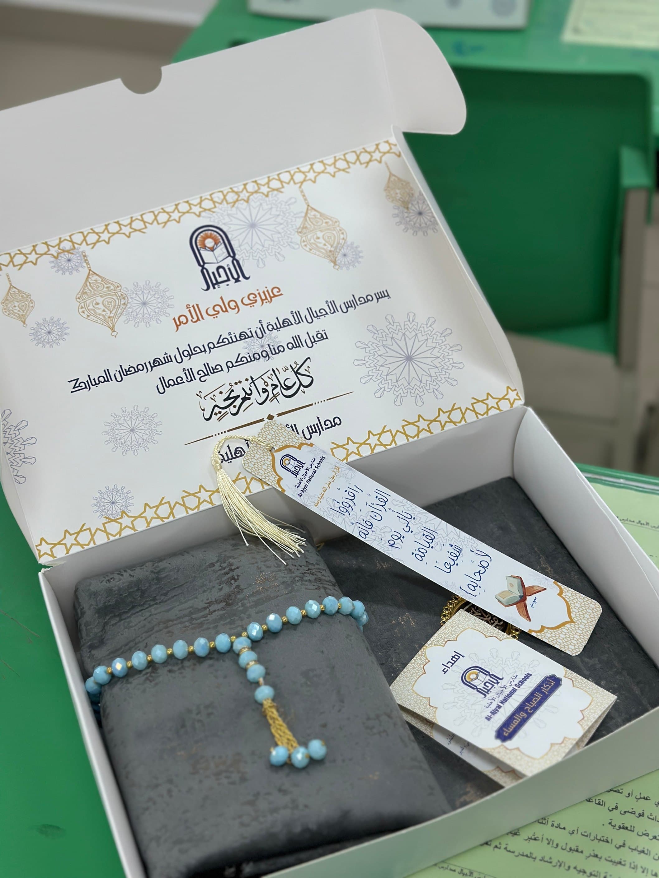 Opened Ramadan gift box with a printed insert card, folded textile and prayer beads laid in the tray