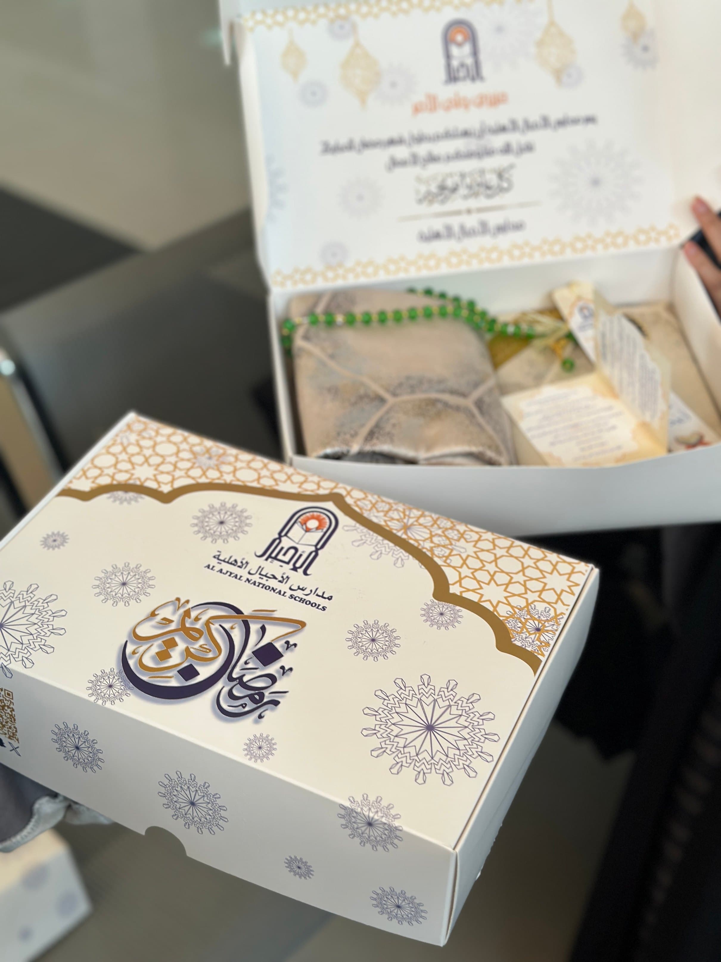 Seasonal Ramadan gift box held in hand: printed lid with Arabic calligraphy and an ornamental border, packed with wrapped contents