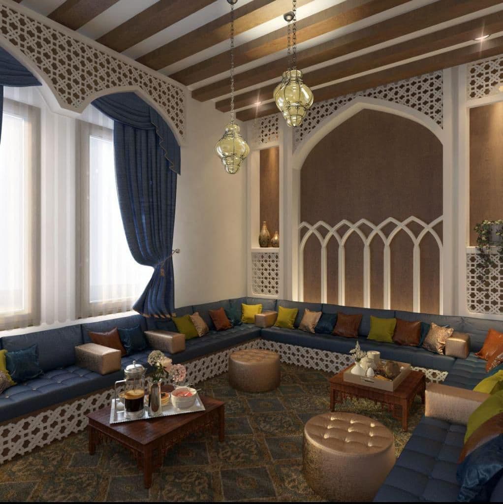 Traditional majlis with a carved plaster screen and arched niche, blue perimeter floor seating and low timber tables
