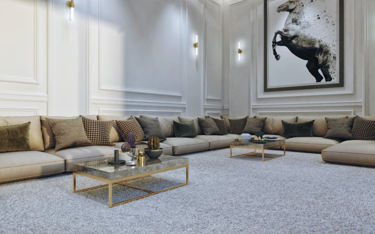 Wide neutral majlis: perimeter banquette with patterned cushions, brass-and-glass coffee tables and framed artwork